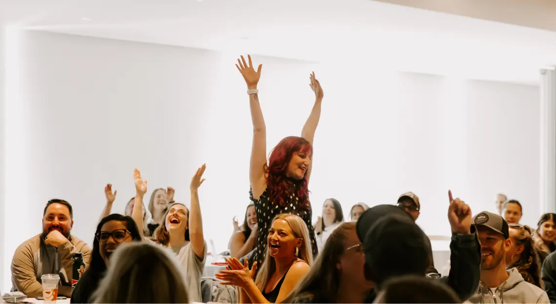 Cheerful woman with hands up surrounded by people sitting and clapping