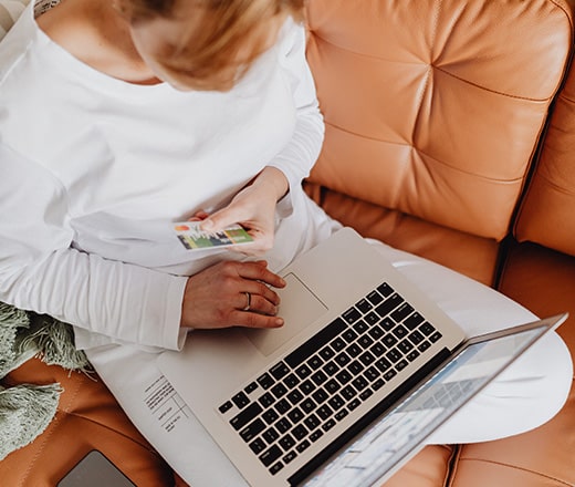 Alt text: Woman on a leather couch with a laptop, holding a credit card while purchasing something online.