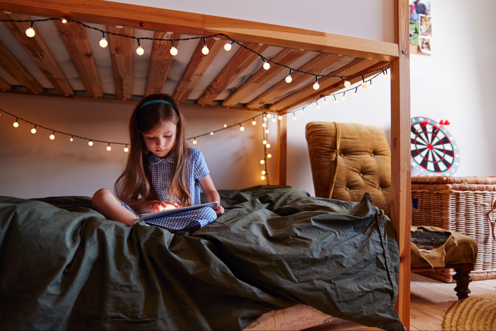 Young girl sitting on a bed at home using a digital tablet.