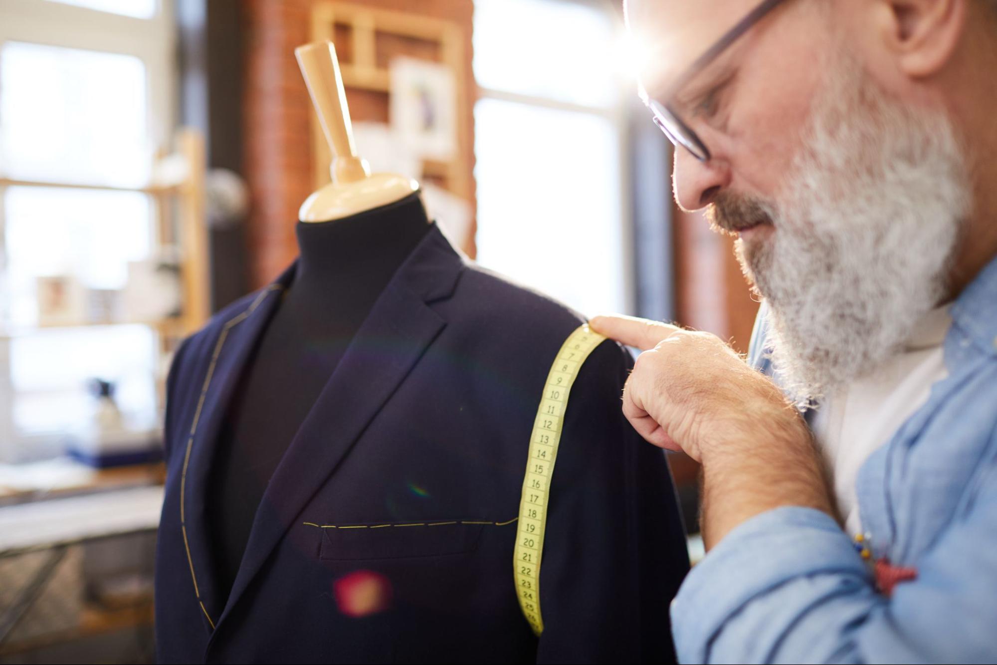 Professional tailor using a measuring tape while altering a jacket in his workshop.