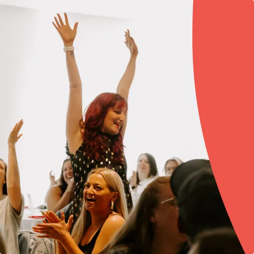 Smiling woman lifting her arms up surrounded with other women sitting and clapping