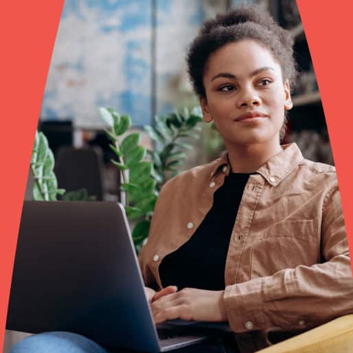 Confident woman sitting and working on a laptop with plants in the background.