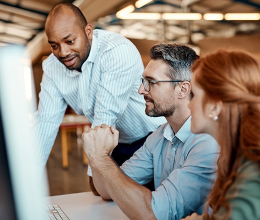 Three focused professionals gathered around a desktop screen in a modern office.