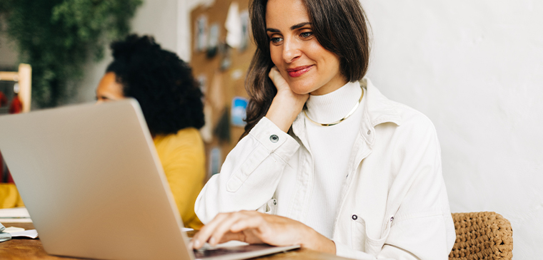 Smiling woman working on a laptop in a sunlit workspace.