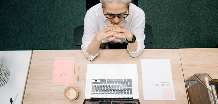 Overhead view of a thoughtful legal professional sitting at a desk with a laptop, coffee, and printed documents.