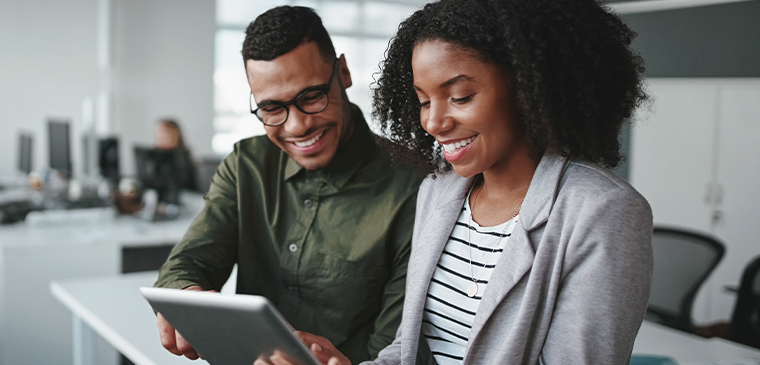 Two smiling professionals standing together in an office, reviewing law firm SEO services on a digital tablet.