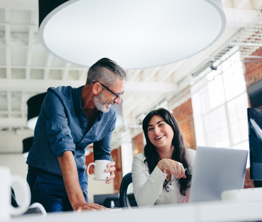 Two colleagues sharing a laugh while working on B2B SEO services together at a computer.
