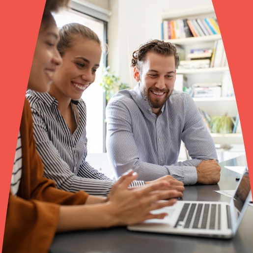 Three SEO colleagues smiling and gathered around a laptop in a well-lit office.
