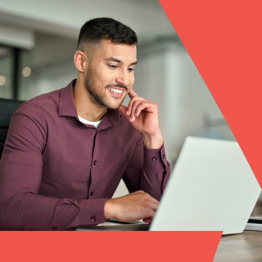 Smiling professional in a maroon shirt working on a laptop in a bright office.