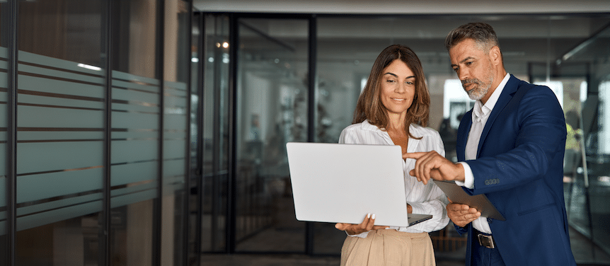 Two professionals in business attire reviewing content on a laptop.