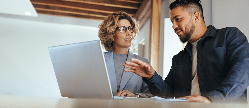 Two professionals collaborating at a desk, reviewing SEO strategy on a laptop while discussing strategy.