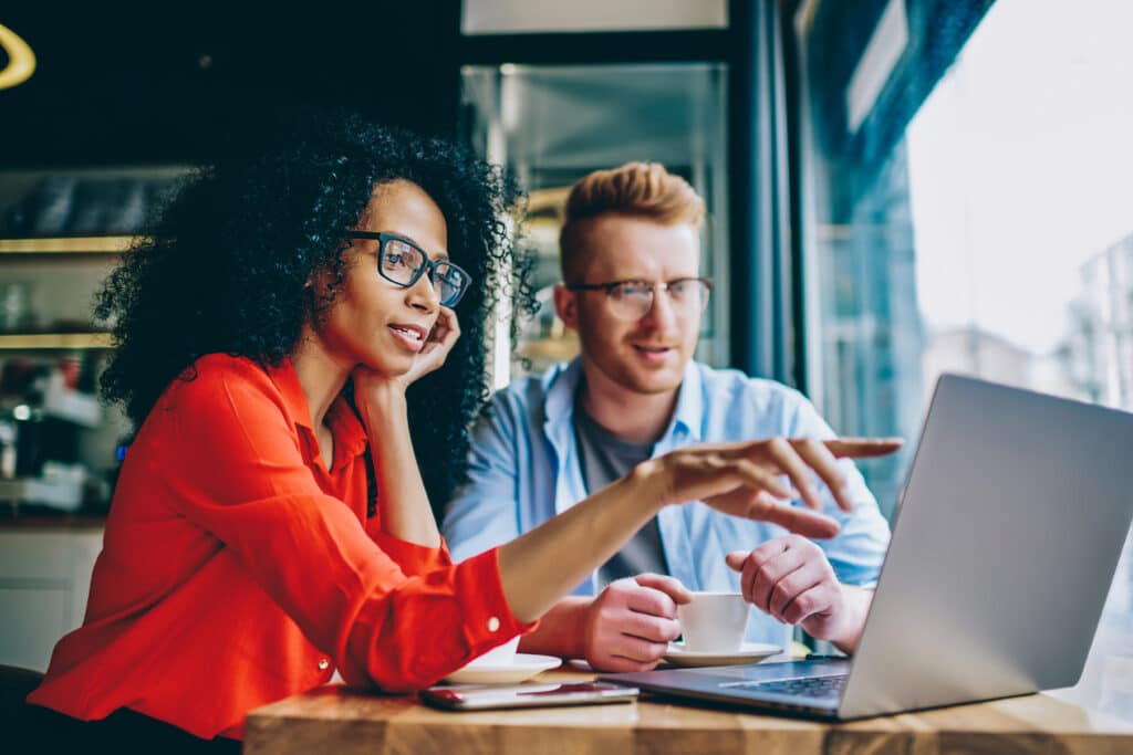 female coworker shows AEO metrics to male coworker on laptop