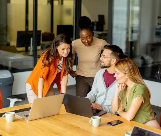 Group of colleagues gathered around a laptop, reviewing SEO migration services in a bright office.